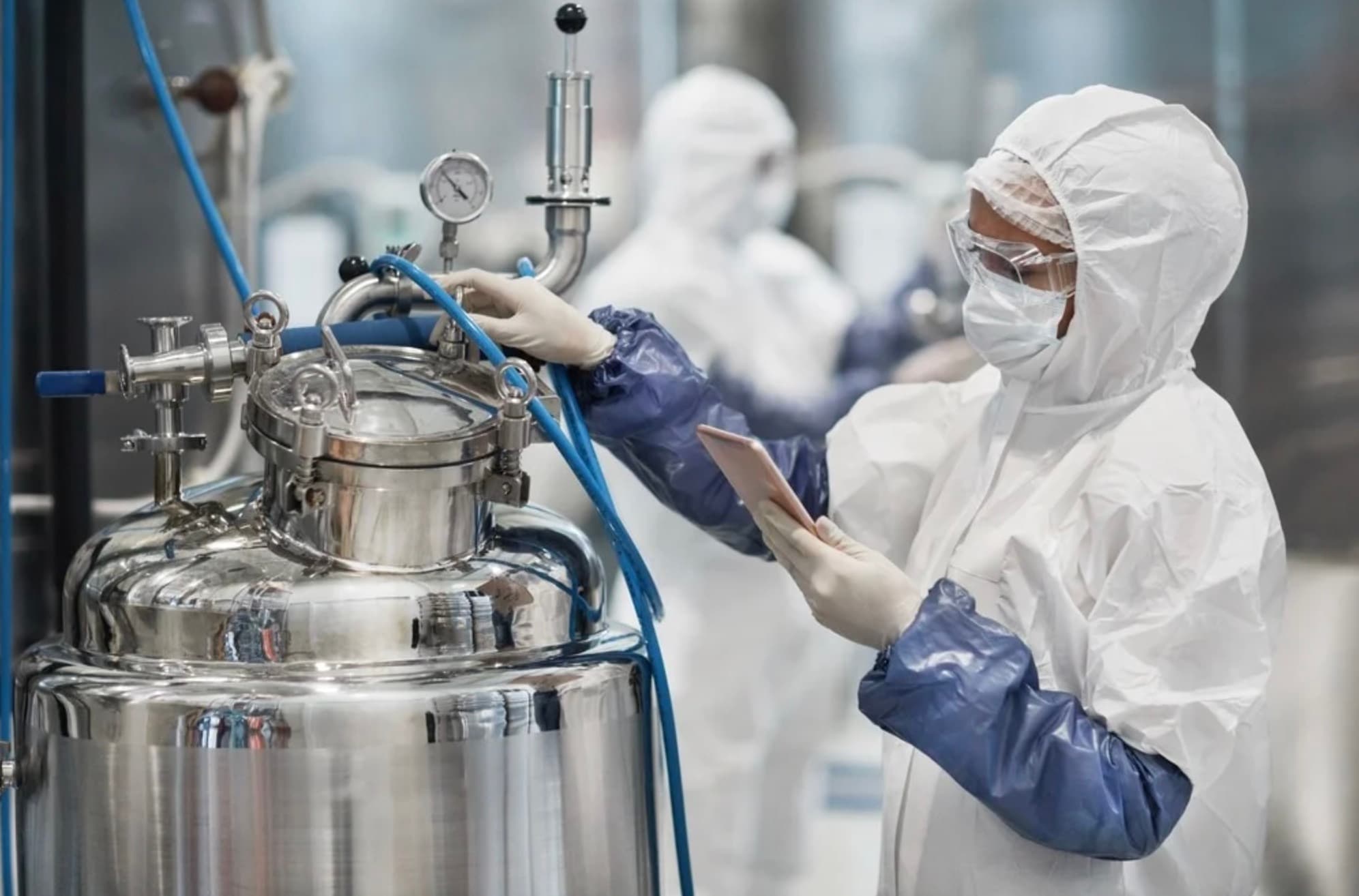 A technician in a cleanroom suit checking a stainless steel process vessel